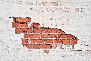 Texture of an old brick wall with damaged plaster and cracked white paint.