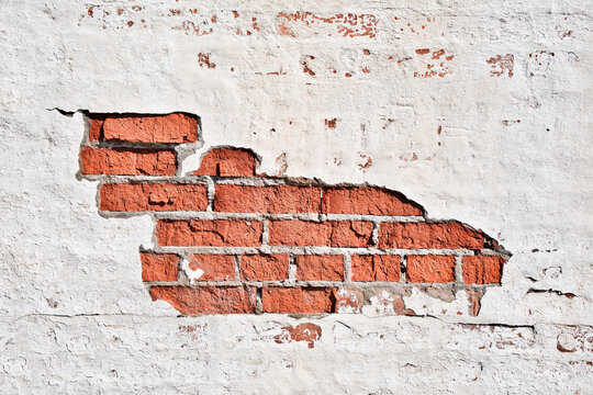 Texture of an old brick wall with damaged plaster and cracked white paint.
