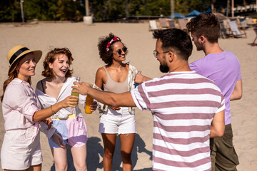 Group of friends walking together on the beach. They are drinking colorful cocktails and having fun.