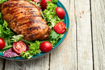 Grilled chicken breast ( fillet ) with lattuce salad and cherry tomatoes . Top view