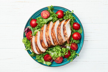 Grilled chicken breast ( fillet ) with lattuce salad and cherry tomatoes . Top view