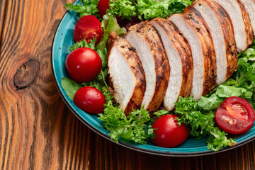 Grilled chicken breast ( fillet ) with lattuce salad and cherry tomatoes . Top view