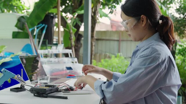 Asian woman programming microcontroller to control analog dissolved oxygen sensor. Using electric meter to monitor microcontroller operation. Agriculture and aquaculture. Internet of Things (IoT)