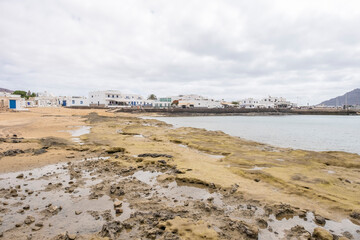 Caleta del Sebo beach, a picturesque white village on the island of La Graciosa in Canary Islands, with its shops and docks in the background, horizontal