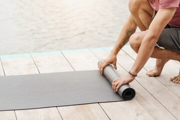As the sun rises, an individual rolls up a yoga mat on a wooden dock beside a calm body of water, embracing a moment of tranquility and focus.