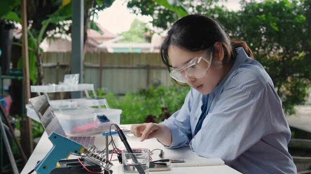 Asian woman programming a microcontroller to control an analog dissolved oxygen sensor and display the results on a smartphone. Agriculture and aquaculture, Internet of Things (IoT).