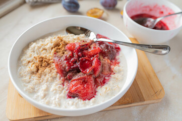 Homemade breakfast porridge with cinnamon and plum compote. Served ready to eat in a bowl with spoon