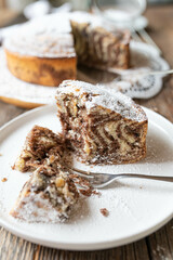 Piece of sponge cake with zebra pattern on a plate with fork on wooden table background