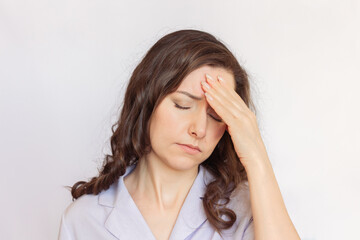 Young brunette businesswoman with curly hair wearing a purple blouse has health problems, suffers from migraine, holds her head with her hand from fatigue