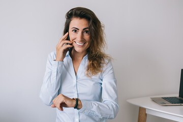 Smiling young woman with wristwatch talking on phone and looking at camera