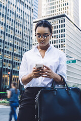 Adult ethnic concentrated lady interacting with smartphone while standing in downtown