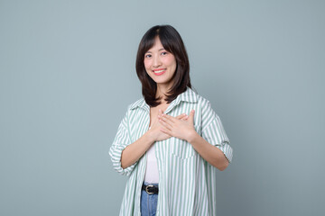A young woman with long hair smiles warmly while placing her hands over her heart, conveying sense...