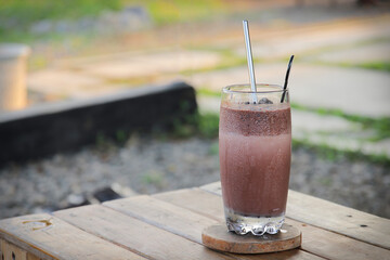 Iced chocolate drink served in clear glass on rustic wooden table. Beverage concept
