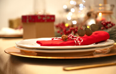 Christmas table setting. Plate with festive napkins and decorations, gifts in the background.