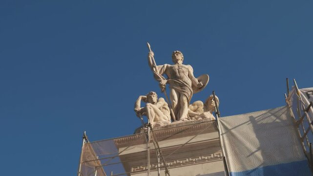 Workers carefully restore a stunning statue featuring a heroic figure and two companions