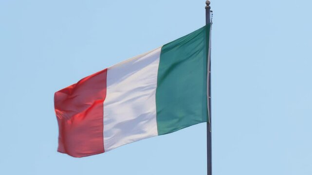 The Italian flag waves proudly in the clear blue sky, a symbol of national pride