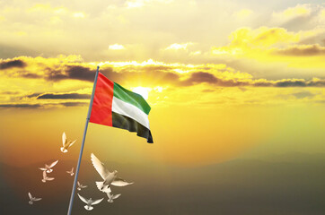 United Arab Emirates flag waving with flying doves against sunset or sunrise. United Arab Emirates flag for Republic Day and Independence Day.
