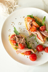 plate of bruschetta with duck breast, arugula and cherry tomatoes on table, top view