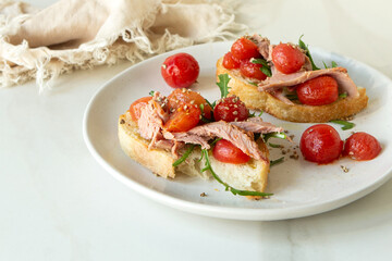 plate of bruschetta with duck breast, arugula and cherry tomatoes on light table