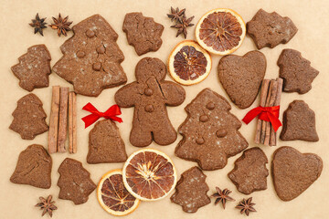 Christmas gingerbread cookies or biscuits on baking paper, winter seasonal traditional bakery with spices, dry orange, cinnamon sticks, anis, candy. Top view sweet food pattern, new year flat lay