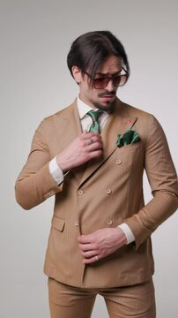 attractive businessman walking forward while fixing his double breasted brwon suit and glasses then turning back