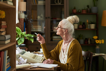 Senior woman with white hair tied up, holding cigarette, working in an office environment with books, plants, and retro technology surrounding her
