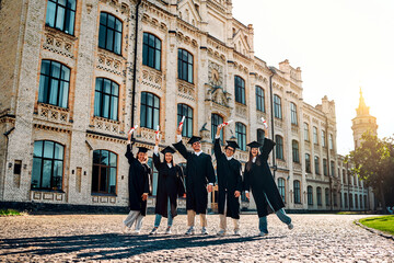 Joyful students celebrate graduation. Graduates stand near the university and raise their diplomas....