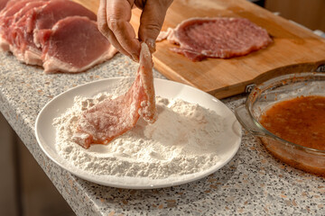 Cook dips pieces of beaten meat fillet in flour before further frying in a frying pan