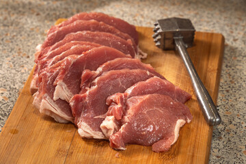 Pork chops from fresh raw meat, sliced ​​and beaten with a kitchen meat mallet, lie on a wooden board. Close-up