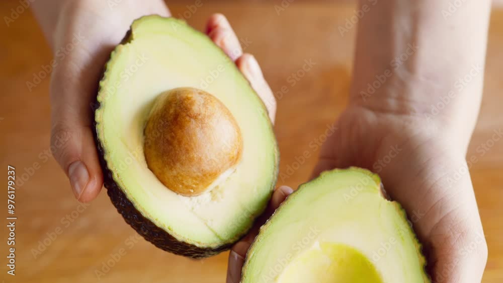 Sticker female hands opening ripe cut avocado on two halves, close up