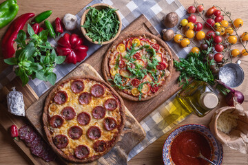 Making pizza with salami, cheese, sauce, tomatoes, vegetables and fresh herbs on wooden background. Top view