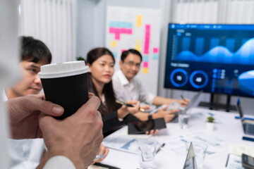 Businessman holding coffee cup while working on data analysis meeting, analyst team analyzing business intelligence or BI dashboard power for business insight and marketing planning. Prudent