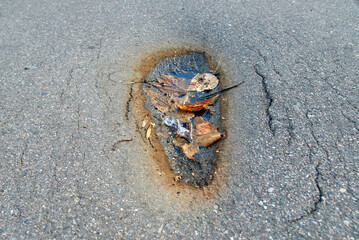 Asphalt road cracked and collapsed from above. Depression in asphalt surface caused by subgrade settlement. Road dent, damaged asphalt, cracking in older asphalt pavements. 