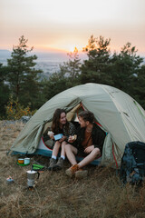 Smiling young man and woman having dinner near a tent in the mountains at sunset.
