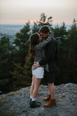 A couple in love embrace while standing on the edge of a cliff at sunset.