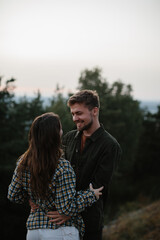 A couple in love embrace while standing on the edge of a cliff at sunset.