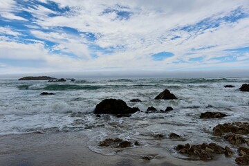 Choppy waves crashing around scattered rocks in the ocean, creating a dynamic and rugged seascape.