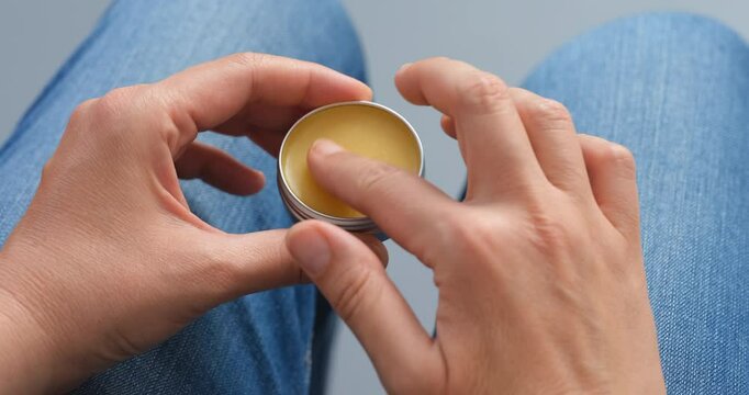 Woman applying balm to her index finger from a tin can