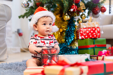 Baby in red hat on Christmas Day, filled with camera, presents and Christmas tree.