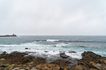 Sous un ciel couvert, les amas rocheux bordent la mer d'Iroise le long de la route touristique de Landunvez en Bretagne, avec de petites vagues et de l'écume blanche.