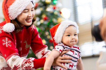 Baby in red hat on Christmas Day, filled with camera, presents and Christmas tree.