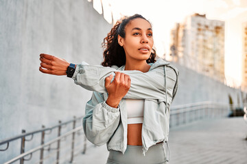 Attractive female runner stretching hands at street. Woman exercising outdoors in the morning.