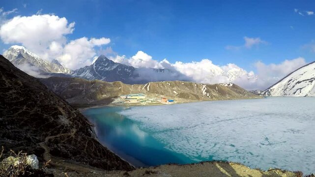 Panoramic view on Gokyo mountain valley with ice partly covered Gokyo lake and Gokyo village in Nepal in Himalayas on height 4750 meters in a sunny day. Time lapse video. Landscapes theme