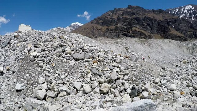Panoramic side view of Ngozumpa glacier covered with ice and large stones and rocks in Himalayas in a sunny spring day. Cholatse mountain peak in the background. Handheld video. Extreme terrain