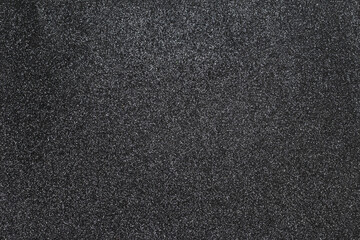 Black paper with glitter and sprinkles. Rough texture effect with sparkles. Photography