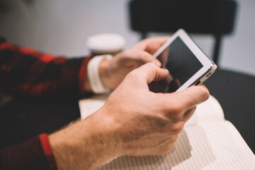 Crop man using tablet and notepad for work