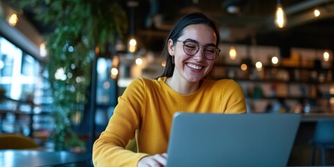 Fototapeta premium A young woman, wearing glasses and a yellow sweater, is deeply engaged with her laptop in a trendy and vibrant cafe, immersed in her digital world.