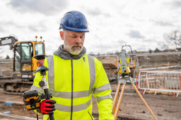 Construction Worker Using Surveying Equipment on Cloudy Day at Building Site