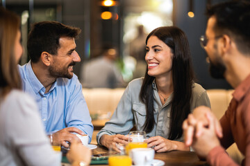 Group of friends met at the cafe. Drinking coffee and orange juice. Girl and guy are talking while the other friends are listening to them.