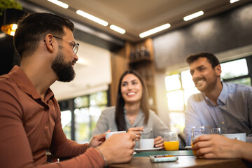 Group of friends laughing together at the coffee shop. They drink orange juice and hang out together.